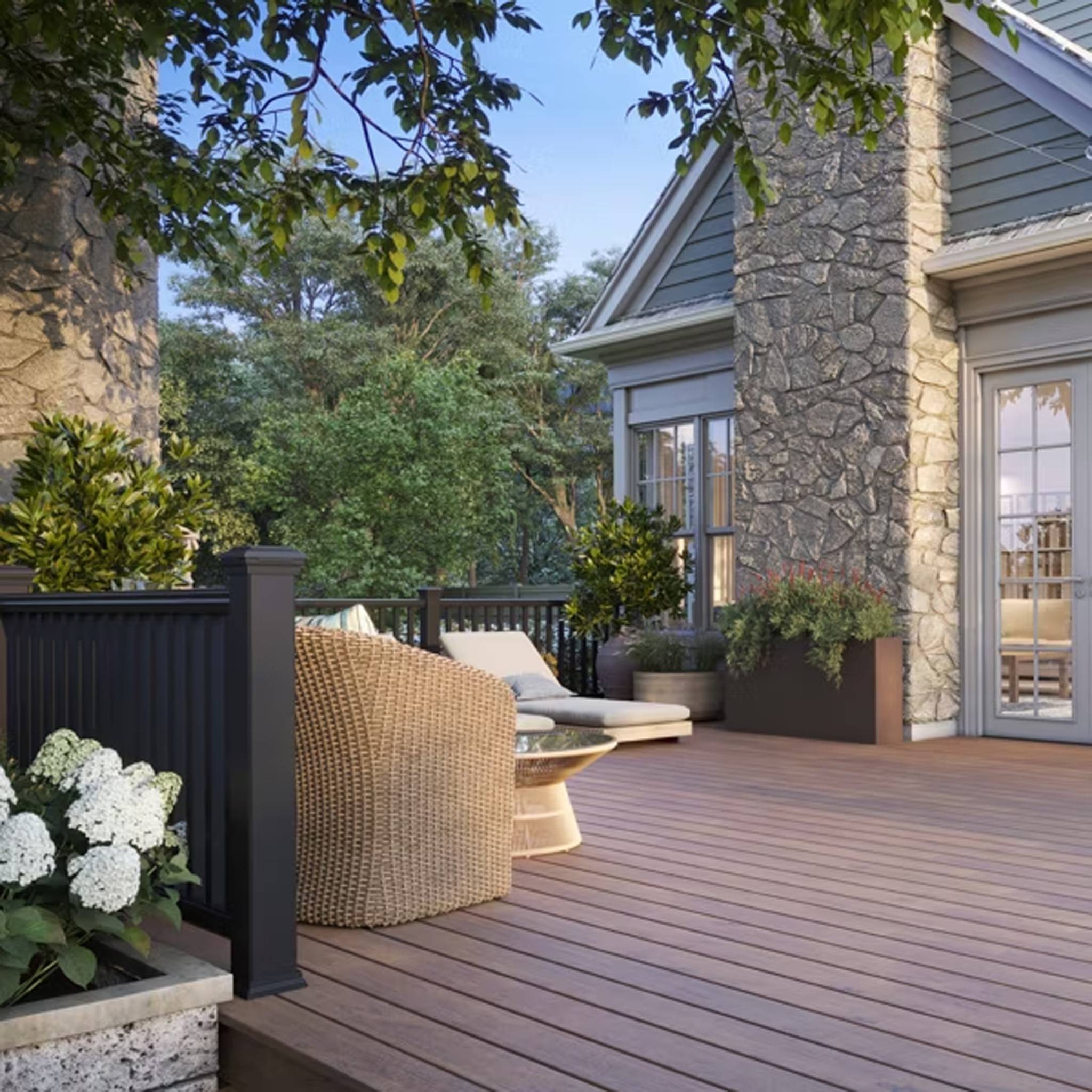 Beautiful outdoor deck with Trex Lineage Hatteras decking, complementing a cozy seating area with stone fireplace and lush greenery. This composite deck blends durability with a natural wood-like aesthetic.
