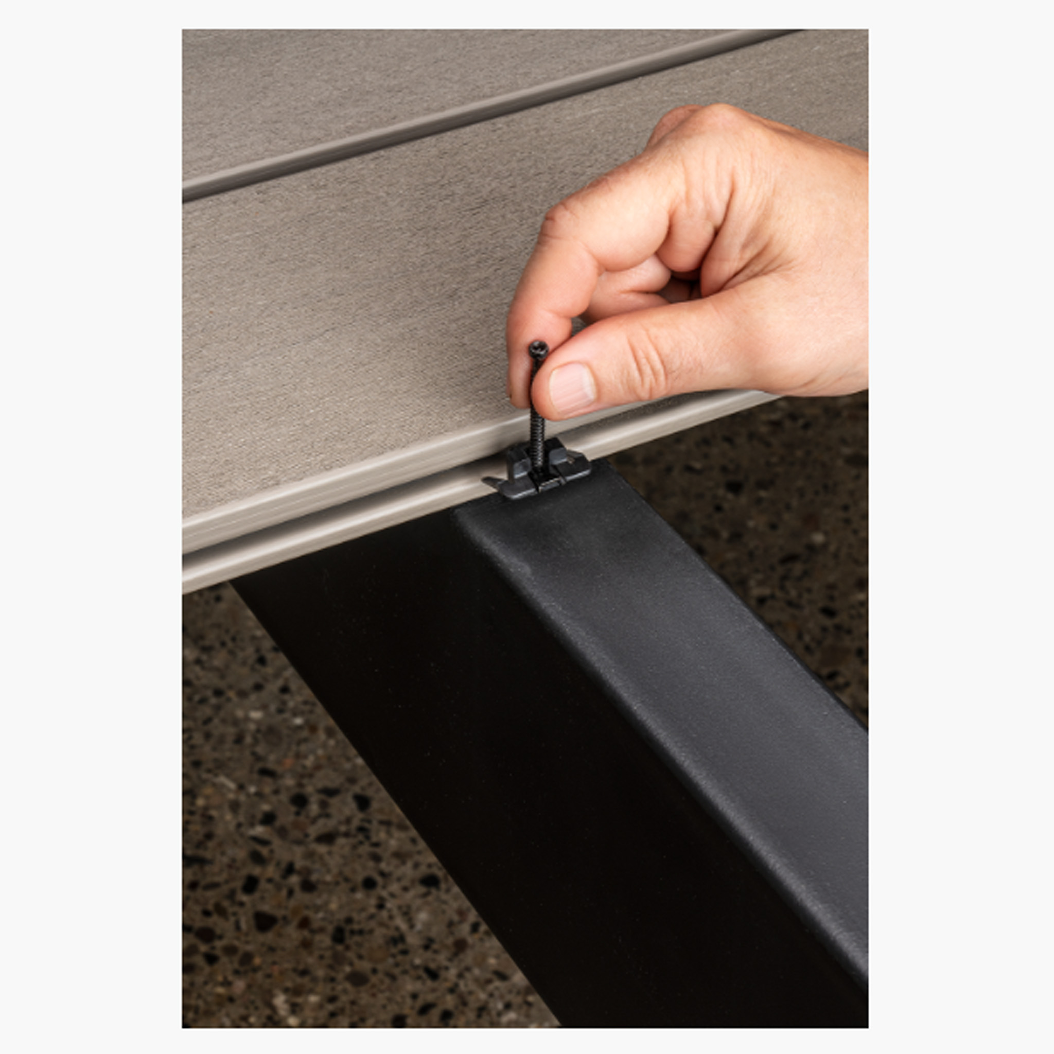 Hand placing a CAMO Wedge Metal Clip onto a metal deck joist, securing a grooved deck board in place.
